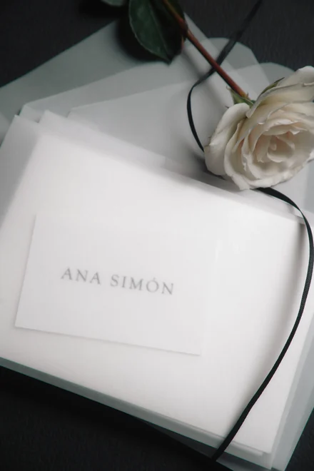 Sobre de papel vegetal con la tarjeta de Ana Simón, una cinta negra y una rosa blanca